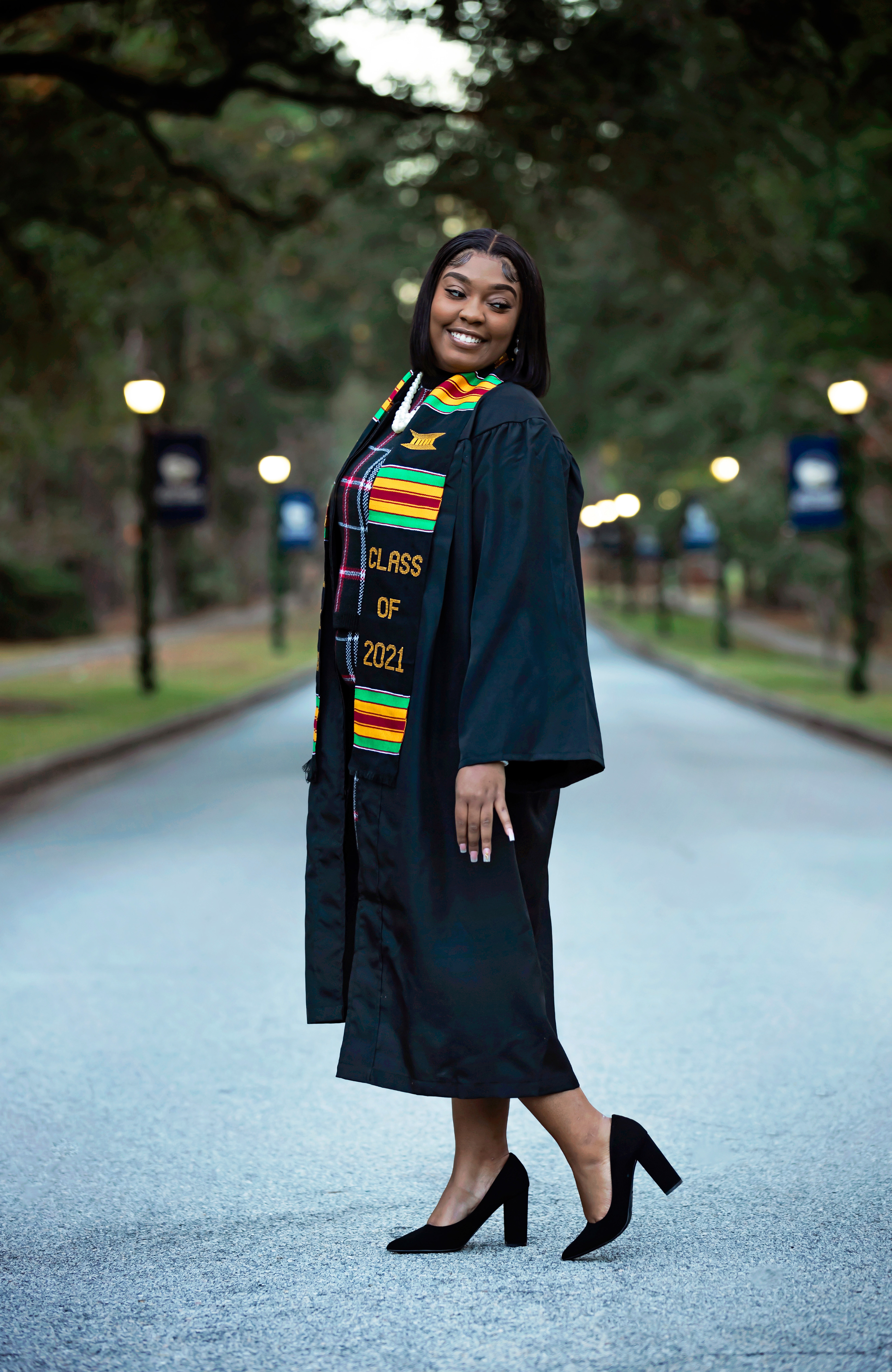 Graduate stands on the walkway to campus